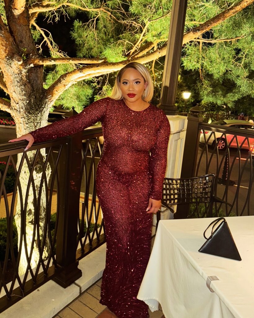 A woman in a long-sleeved, red-wine colored Retrofête sequin dress poses on a patio at night, with a black YSL bag on a table.