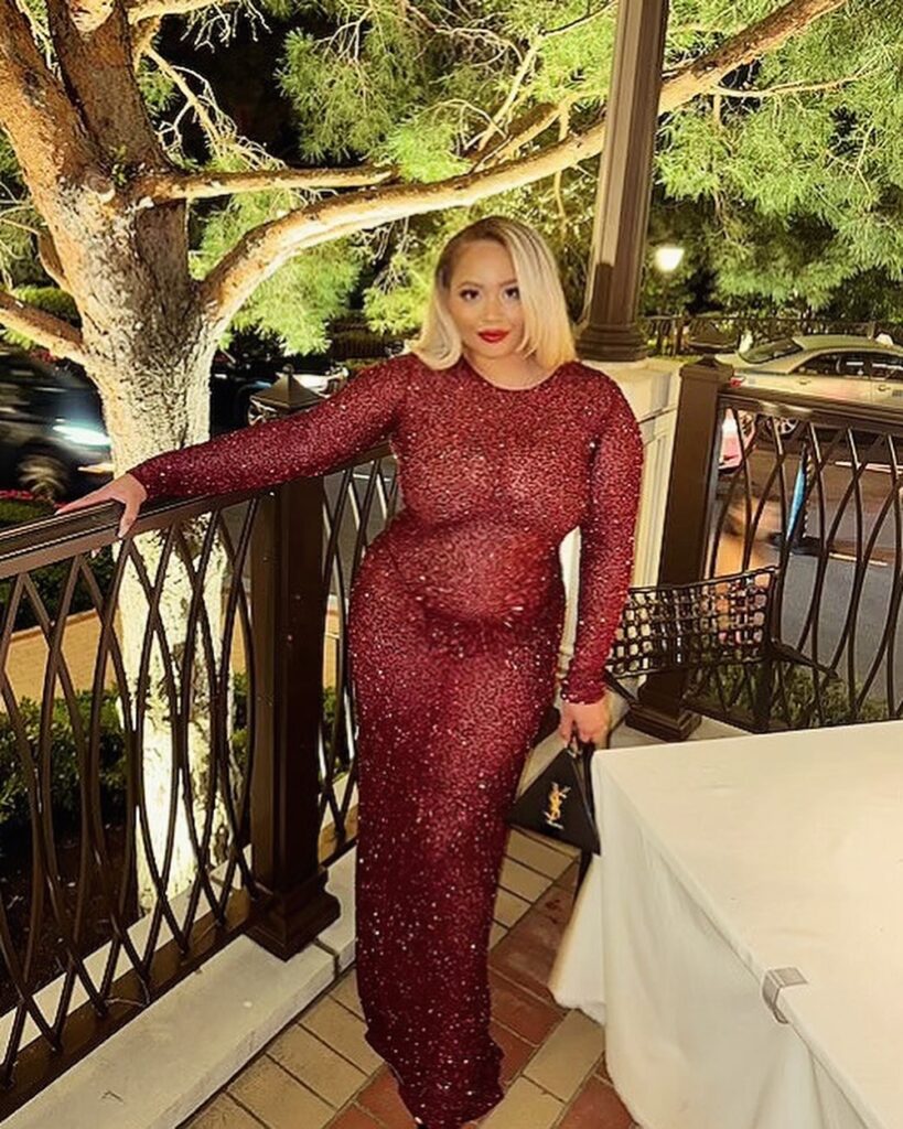 A woman in a long-sleeved, red-wine colored Retrofête sequin dress poses on a patio at night, with a black YSL bag on a nearby table.