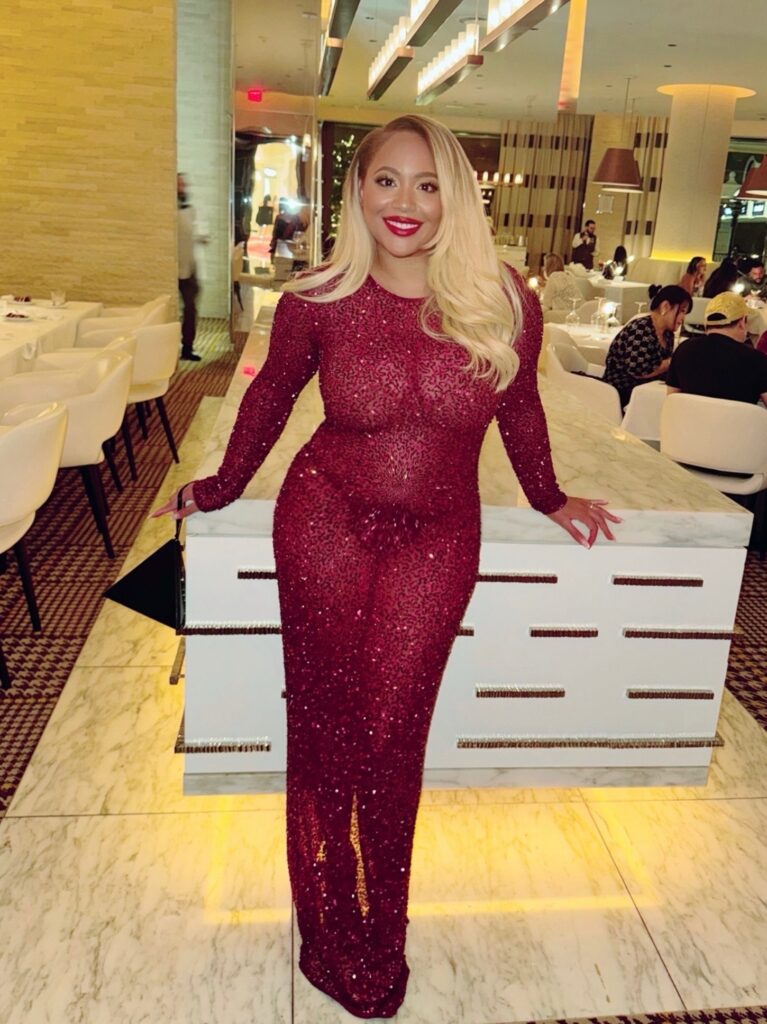A woman in a sequin Retrofête dress stands inside the Rare Steakhouse at Encore Boston Harbor, with her black YSL heels and YSL Pyramid Clutch.